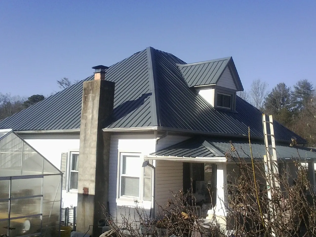 Dark blue standing seam metal roof on a white farmhouse with dormer — Slate & Tile Roof Repair by Roofing Brothers in Rollins