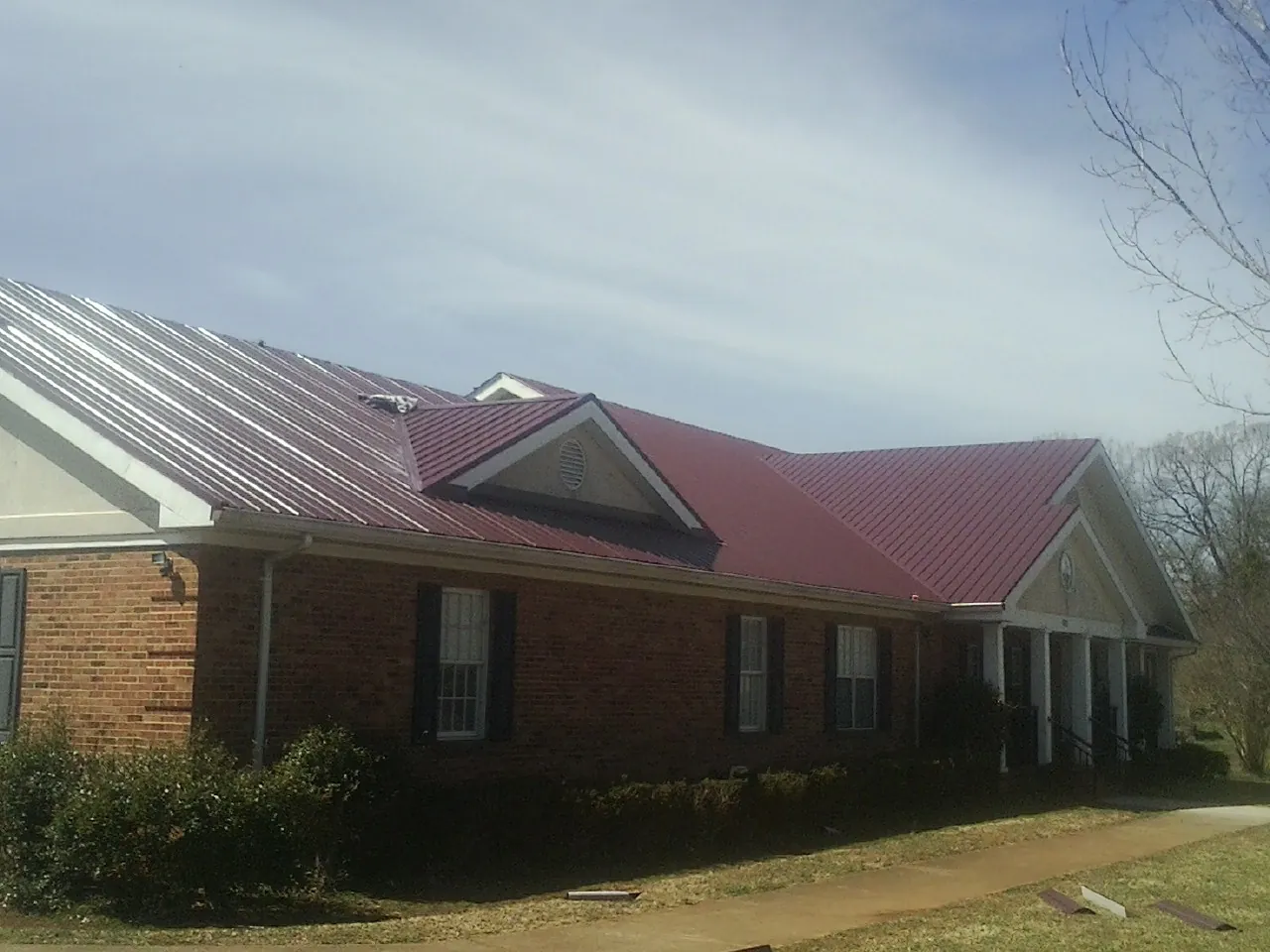 Red metal roof with gabled entries on a long brick building, from a Hail Damage Roof Repair job in Rollins