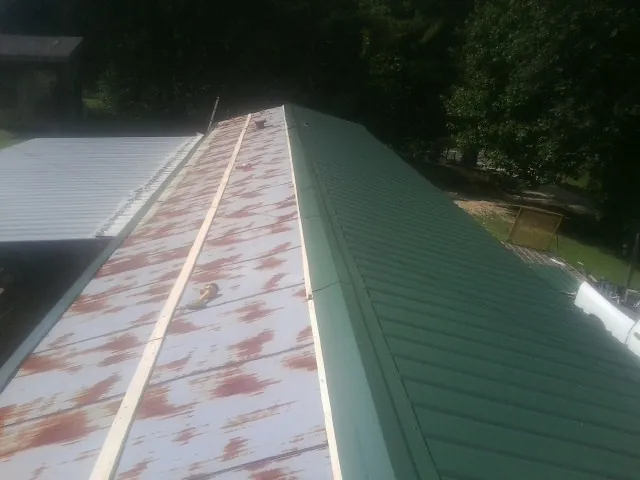 Old rusted panels beside newly installed green metal roofing — Wind Damage Roof Repair by Roofing Brothers in Rollins