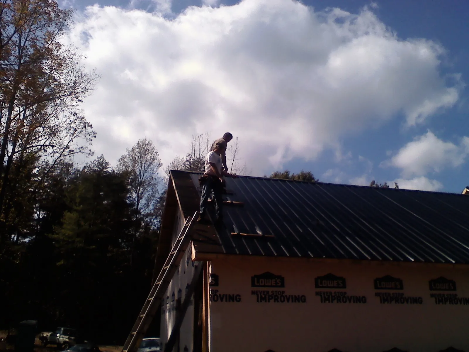 Roofer fastening dark metal panels high against a cloudy sky, from a Roof Inspection job in Rollins