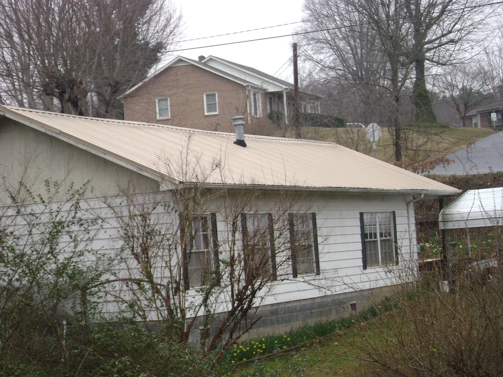 Tan metal roof on a white sided house set into a hillside — Commercial Roofing by Roofing Brothers in Rollins