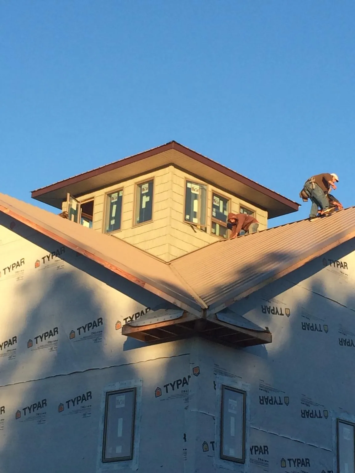 Roofers working around a rooftop cupola on a new metal roof at sunset — Roof Waterproofing in Rollins by Roofing Brothers